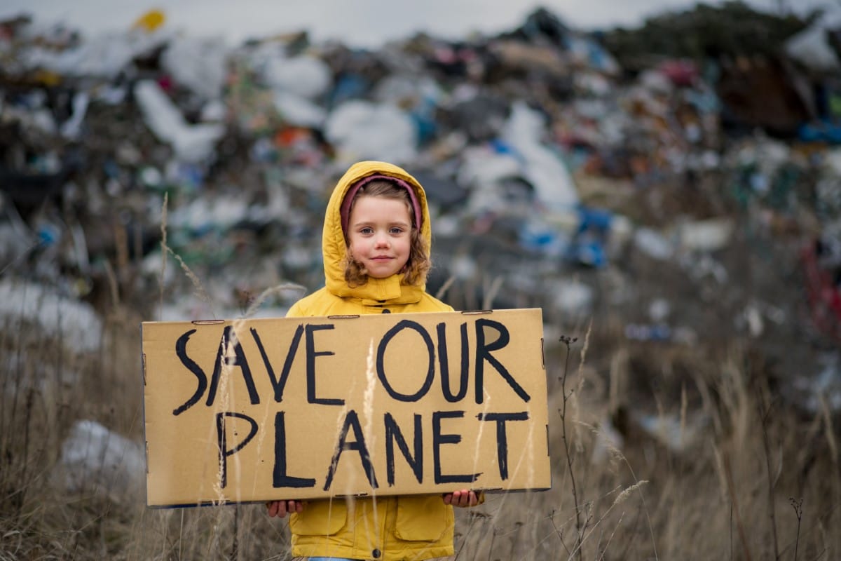 Kind hält ein Schild „Save our planet“ vor einer Mülldeponie
